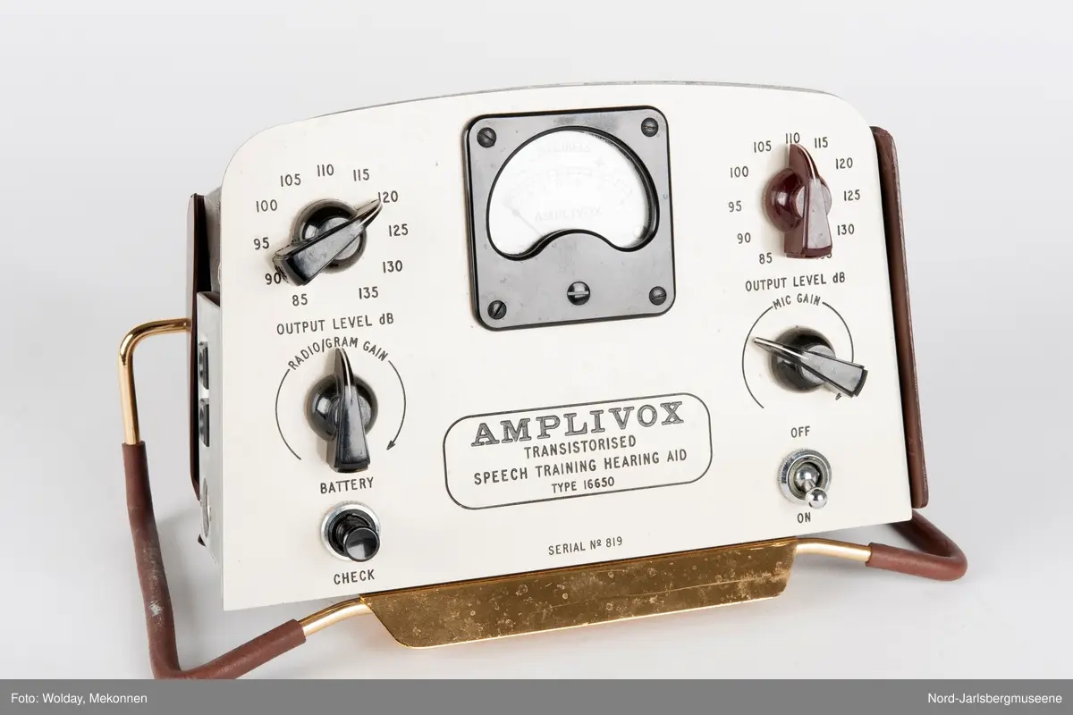 Rektangulært apparat med støtteben i gummipolstret messing (regulerbare). Fronten har målenål, reguløeringsbrytere, av-og-på knapp mm, i bakelitt. Tre uttak for audio på sidn. Bakdekslet i plast er delvis knust, slik at transitorutstyret innvendig er synlig.