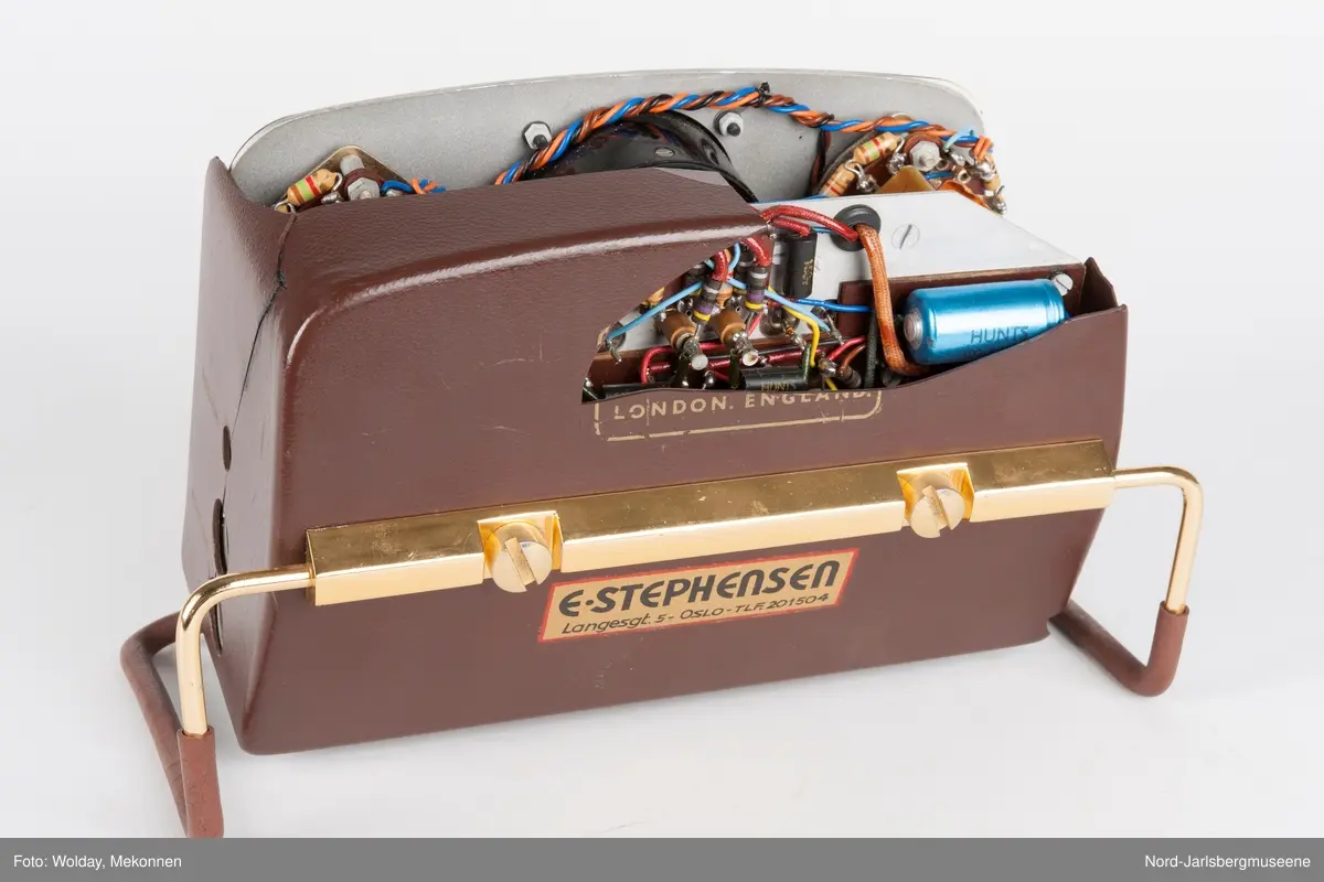 Rektangulært apparat med støtteben i gummipolstret messing (regulerbare). Fronten har målenål, reguløeringsbrytere, av-og-på knapp mm, i bakelitt. Tre uttak for audio på sidn. Bakdekslet i plast er delvis knust, slik at transitorutstyret innvendig er synlig.