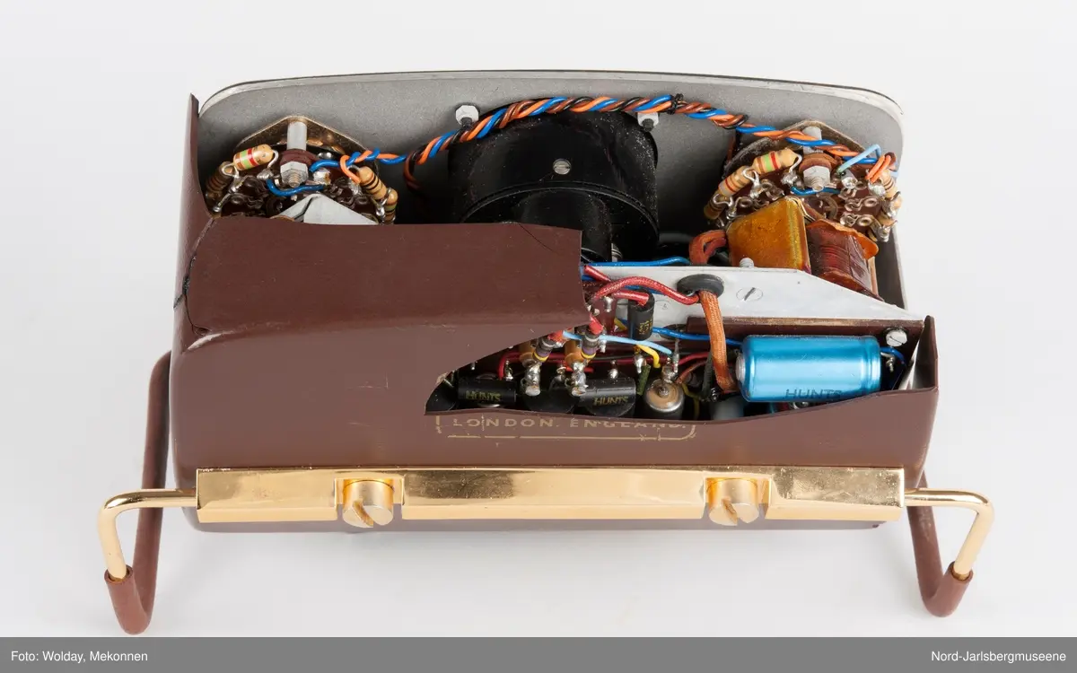 Rektangulært apparat med støtteben i gummipolstret messing (regulerbare). Fronten har målenål, reguløeringsbrytere, av-og-på knapp mm, i bakelitt. Tre uttak for audio på sidn. Bakdekslet i plast er delvis knust, slik at transitorutstyret innvendig er synlig.