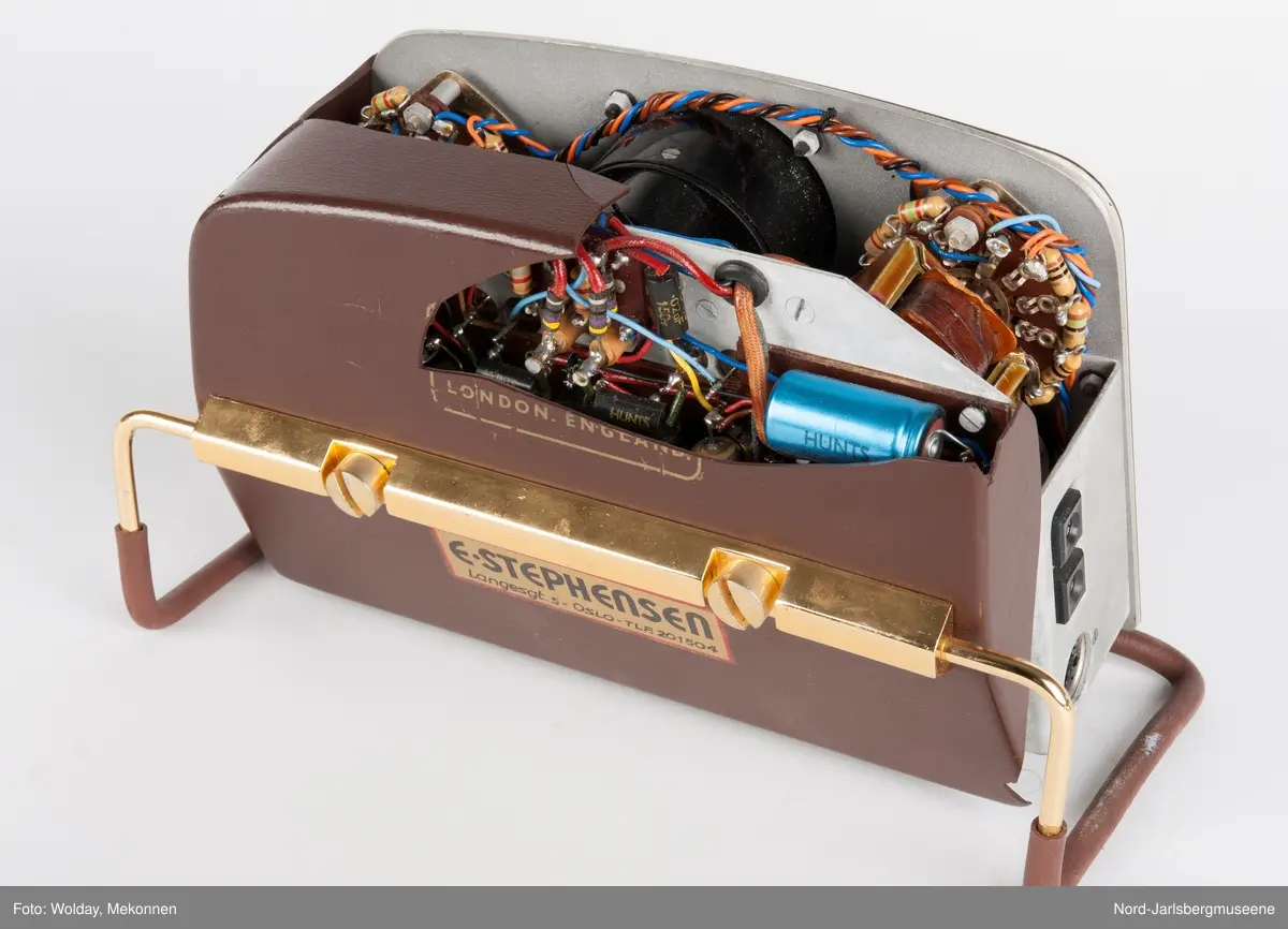 Rektangulært apparat med støtteben i gummipolstret messing (regulerbare). Fronten har målenål, reguløeringsbrytere, av-og-på knapp mm, i bakelitt. Tre uttak for audio på sidn. Bakdekslet i plast er delvis knust, slik at transitorutstyret innvendig er synlig.