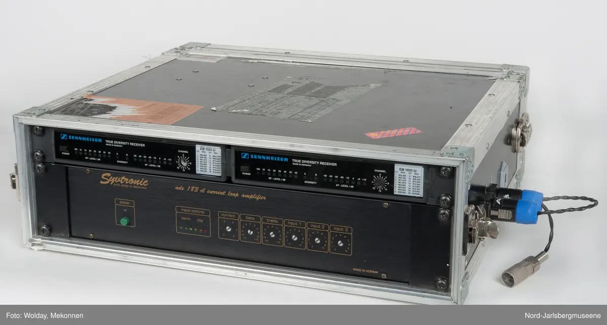 Spesialbygget metallkoffert for audiomåleapparater. Kofferten har åpning på hver ende. På den ene siden finner man måleinstrumenter; to "True Diversity Receiver" og en stor forsterker. I lokket på denne siden er det plass til å oppbevare mindre tilleggsutstyr. Under det andre lokket finner men baksiden av apparatene samt ledninger. Lokket her også plass til ekstra, lange ledninger for kobling til andre apparater. På dene ene langsiden er det tre uttak for koblinger, hvorav en har koblingsledning i.