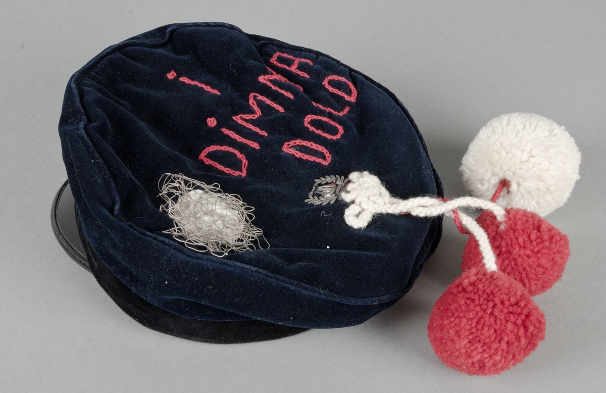 Skolmössa, från sista ring i gymnasiet, av blå sammet med svart sammetsband runt kullen och gul snodd över, skärm av svart lack. Märket med lyra och två lagerkvistar har flyttats bak på mössan och under det är fastsytt tre snoddar med en stor vit  (diam 6 cm) och två mindre (diam 5 cm) runda tofsar av ullgarn. På kullen rund vit applikation och trassel av grå tråd samt broderat med röda kedjestygn: I DIMMA DOLD, på skärmen tre broderade  vita frågetecken av kedjestygn. Invändigt fodrad med ul och blå bomullssatin, plastetikett: Marianne Adolfsson L III:3 Uppsala H.A.L. Brun svettrem.