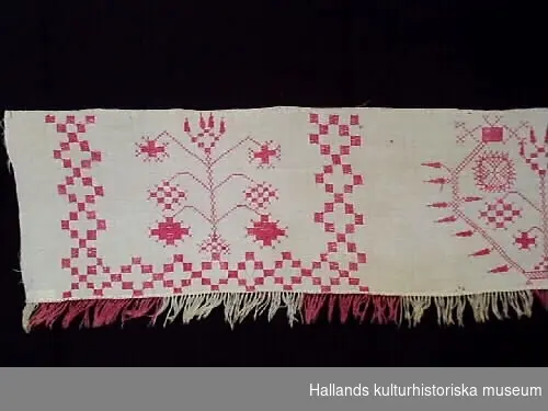 Hängkläde med frans. Vitt med broderier av bomullsgarn i rött och röd och vit frans.