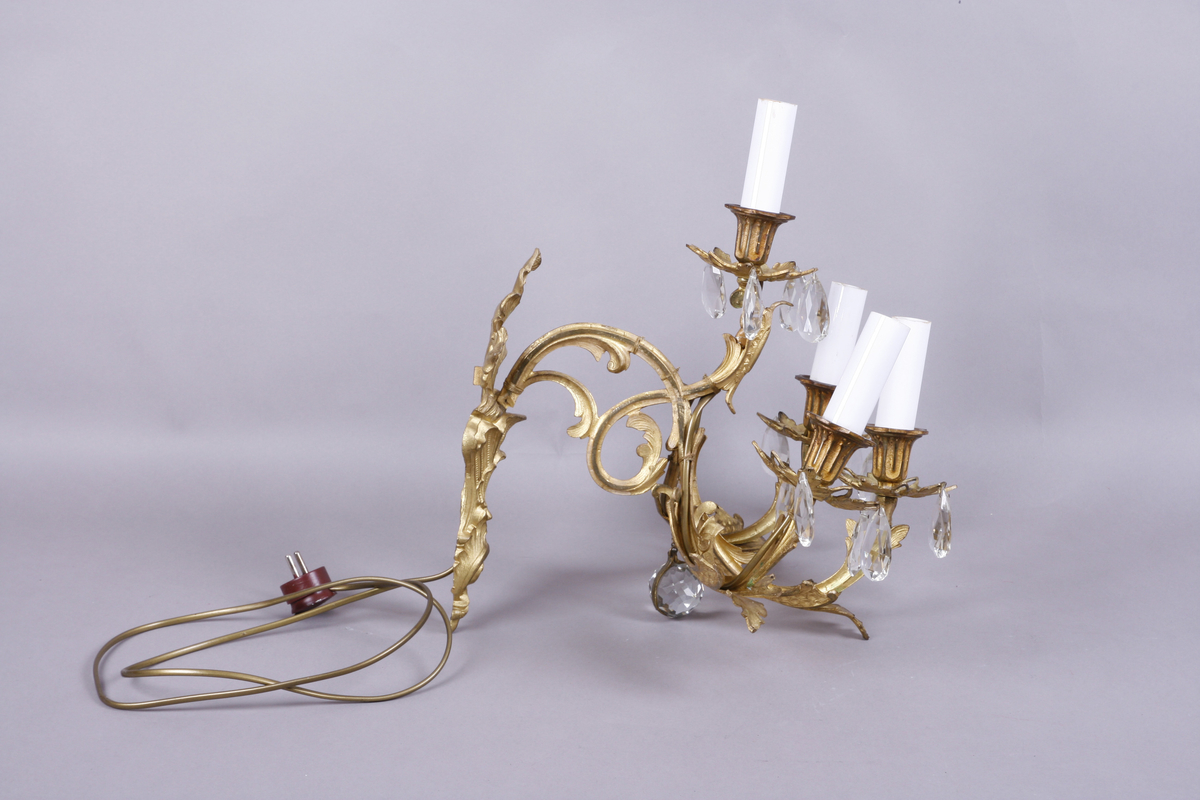 Elektrisk vegglampe med tre armer. Støpt metall. Forgyllet. Påhengte fasetterte glassdråper.