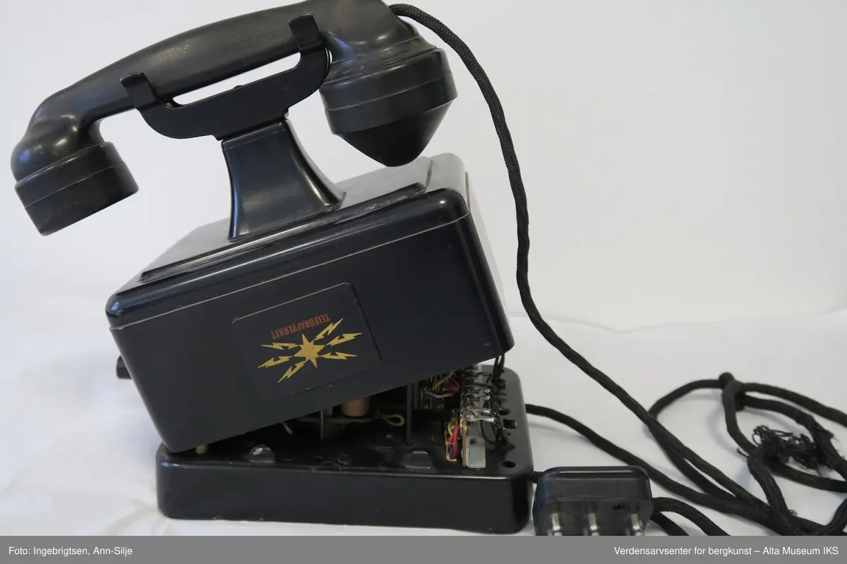 Prismeformet med bæreklo på toppen og telefonrør. Emblem med logoen til Telegrafverket på framsiden av boksen. Boksen er åpnet fra bunnen og er kilt fast slik at det ikke er mulig å lukke den. På baksiden av boksen er det et klistremerke med motiv av Langbein.