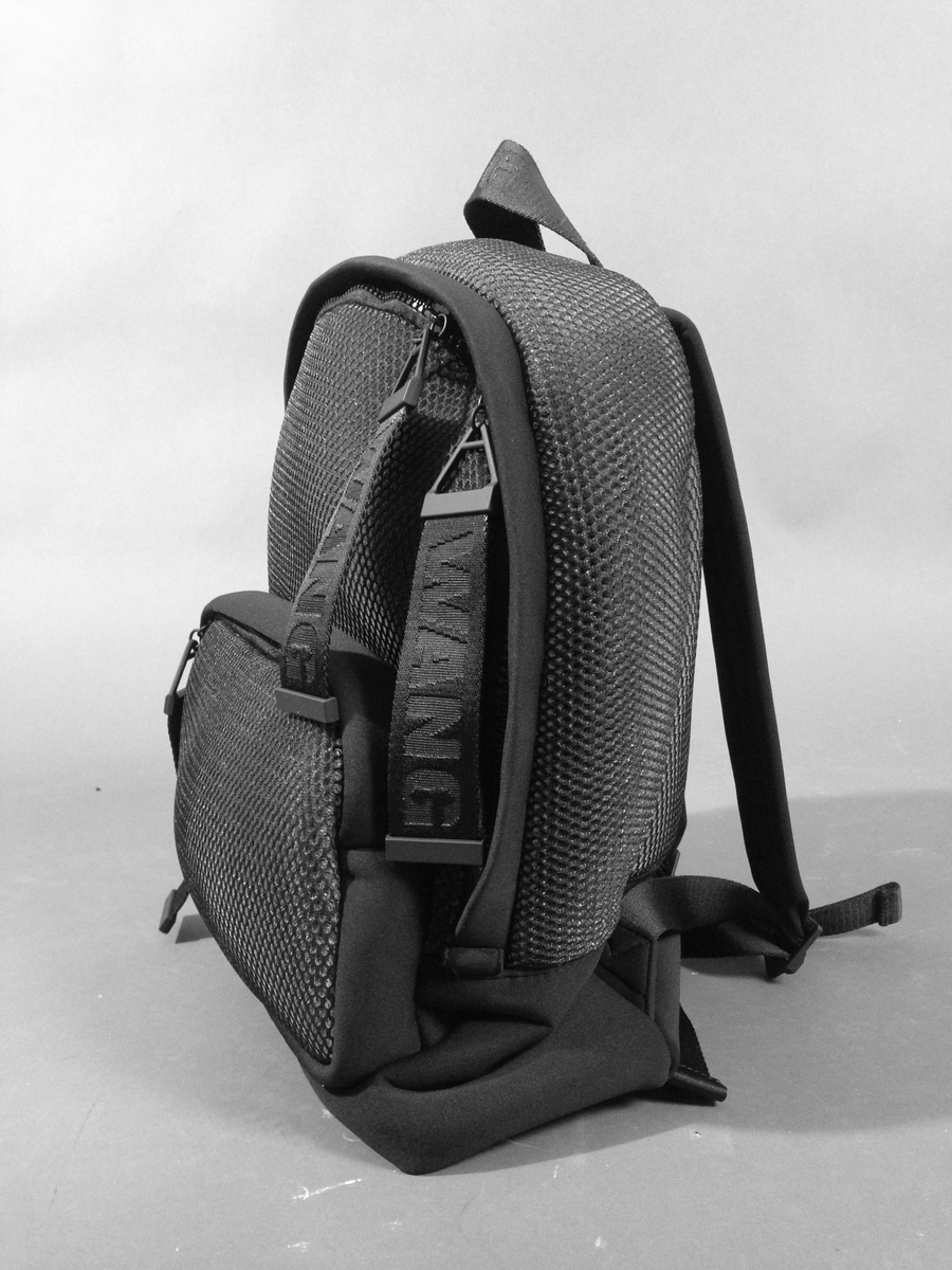 Liten sekk for trening. Sydd av nettstoff, der det ytre stoffet er laminert med flere lag nettstoff, og kjernen antagelig selvlysende, dvs av lysegrå refleksfibre. Sekken består av ett hovedrom og et lite ytterrom. Nedre del av både sekk og ytterrom er av tett neopren. Selve bunnen har en påsydd plate av gummi, med 4 "ben" i form av logoen "AW".  Innvendig bunnplate er imidlertid både bredere og lengre og av ukjente materiale. Sekken er flat nederst og buet i overkant, hovedrommet åpnes nesten helt ned i begge sider og lukkes med grov plastglidelås. Ytterommet åpnes i overkant og lukkes med tilsvarende glidelås. Innvendig er rommene fôret med et ekstra lag, enkelt nettstoff, og hovedrommet utstyrt med en ekstra lomme. Selene er regulerbare med spenner, er polstret, av neopren og utvendig forsterket med påsydde bånd av bevernylonlignende materiale ivevd "WANG" gjentatte ganger. Tilsvarende stropp øverst, til bæring i hånden. Under selefestene en ekstra lomme, lukket med samme grove glidelåstype. Nedi lommen ligger et påsydd regntrekk av tynt, vannavstøtende matriale, med påtrykt "AW" i et sammenhengende mønster utført i lysreflekterende trykkfarge over det hele. Med påsydd elastikk langs ytterkanten, kan trekket raskt tas ut og vikles omkring sekkens front og holde seg på plass i regnvær. Alle glidelåser er utstyrt med en "drastropp" av det sorte bondet ivevd WANG.