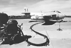 Flygplan J 29 Tunnan tillhörande F 3 Malmen tankas på F 4 Frösön flygfält. Kanslihuset med sitt valmade tak och värmecentralens skorsten syns i bakgrunden.