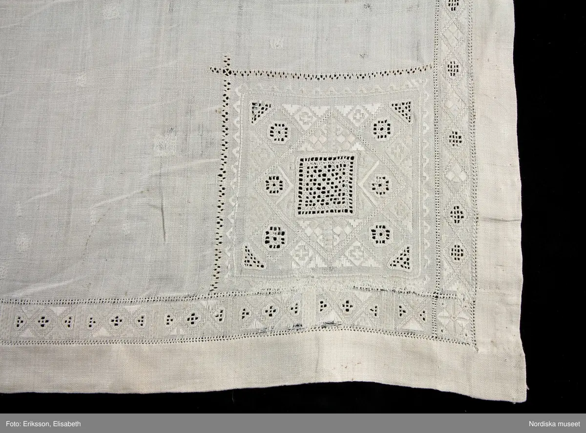 
Katalogkort:
Inga ytterligare uppgifter.

Kvadratiskt kläde i fint handvävt tuskaftat linnetyg, broderier i vitt lingarn. En 2,3 cm bred broderad kantbård  följer alla sidor. Kvadratiska hörnbroderier, 13 x 13 cm, i alla hörn. Broderierna består av rombiska, kvadratiska och trekantiga former. Utdragssöm i kanterna av bården och hörnboderierna. Broderierna utförda i rätlinjig plattsöm, utskuren söm och enkel utdragssöm.På baksidan sitter i tre av hörnen  en lagetterad hank  avsedd att fästa de dinglande hörnbroderierna i. 
Anm. Klädet har  på åtskilliga ställen stoppats  med sytråd.
Har enligt givare tillhört hennes mors faster Elin Hertzman som på 1880-talet hade gästgiveriet i Broby. Hon har enligt givaren själv, odlat, spunnit och vävt linnet. 
 Det förefller dock troligt att detta kläde har tillhört en äldre generation innan Elin H. ägde det.
Utdrag ur Svensson Sigfrid, (1935). Skånes Folkdräkter, en dräkthistorisk undersökning 1500 - 1900. Stockholm: Nordiska Museets Handlingar: 3, sid. 262 - 263: "Härmed kan sammanställas Linnés uppgift från Göinge: 'Torrklädet' är et linne armkläde, wid kanterna genombåradt och sydt samt med spetsar kantadt och med wippor i hörnen utsiradt'. Dessa benämningar - 'näsduk', 'torrkläde' och 'armkläde' - förekomma i bouppteckningarna redan vid 1700-talet början och åsyfta tydligen då en duk, som burits på armen eller hållits i handen...Från Ö. Göinge omtalar Eva Vigstsröm, att till fästmögåvorna också hörde en 'kinnaklud' och enligt beskrivning var denna av fullkomligt samma utseende som armklädet. Om dess användning säges: 'Denna klut bands helt utbredd öfver brudens hår, då hon red eller åkte till kyrkan.' Samma bruk har förekommit i Ingelstad: 'Under resan till och från kyrkan hade bruden öfwer locken, liksom öfwer kluten, ett 'hyeklä', ett fyrkantigt tygstycke af linne med genombrutet arbete.'. Enligt Wistrand användes samma plagg även vid kyrkobesök och resor och Svanander omtalar hyeklädets användning till sorgdräkten, fig 242. Att armkläde och hyekläde förkomma samtidigt i bouppteckningarna torde bero på en senare differentiering. Ett och samma slags linneduk har kunnat användas som förningsduk, 'bokkläde' och 'gudmoraklut' (som bars av faddrarna ovikt och fäst under hakan på samma sätt som hyeklädet)."
Lästips: Håkan Nilsson, Röepäls, klut och skörtatröja, s. 28-41.
Östelens folkdräkter, Ystadiana 2000.  Ystads Formninnesförening. Ystad 2000.
/Berit Eldvik 2010-10-18