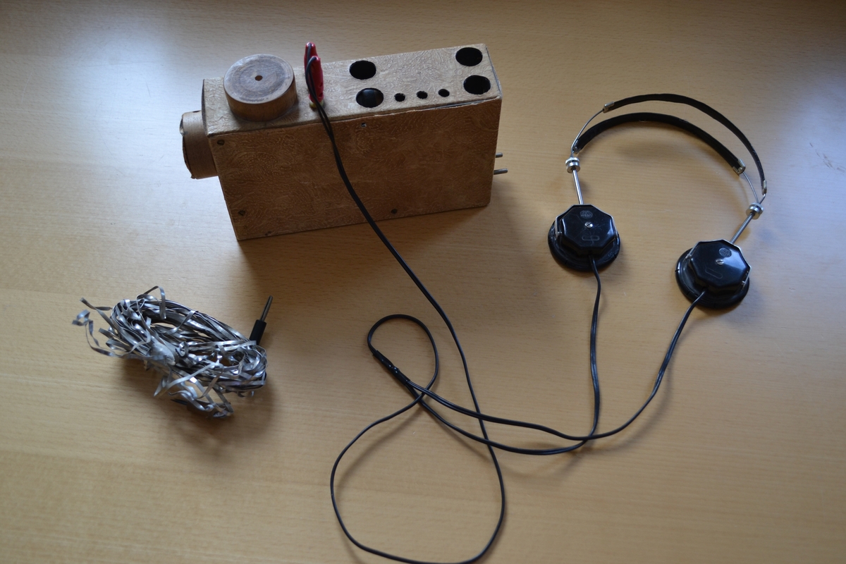 Radiomottaker, hjemmelaget. Rektangulært chassi laget i trefiner.. Med sorte høretelefoner med stempel OMEGA. Dette eksemplaret er fortsatt i utmerket stand. Det følger også med en improvisert antenne.