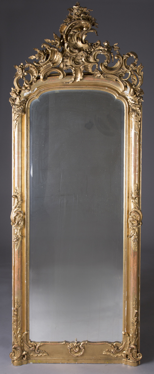 Stort, rektangulært speil med utskjæringer på rammen. Forgylt ramme. Rocailler i asymmetrisk mønster. Speilet buer seg lett ved toppstykket. Rikt asymmetrisk utskjært toppstykke med blomster og rocailler.