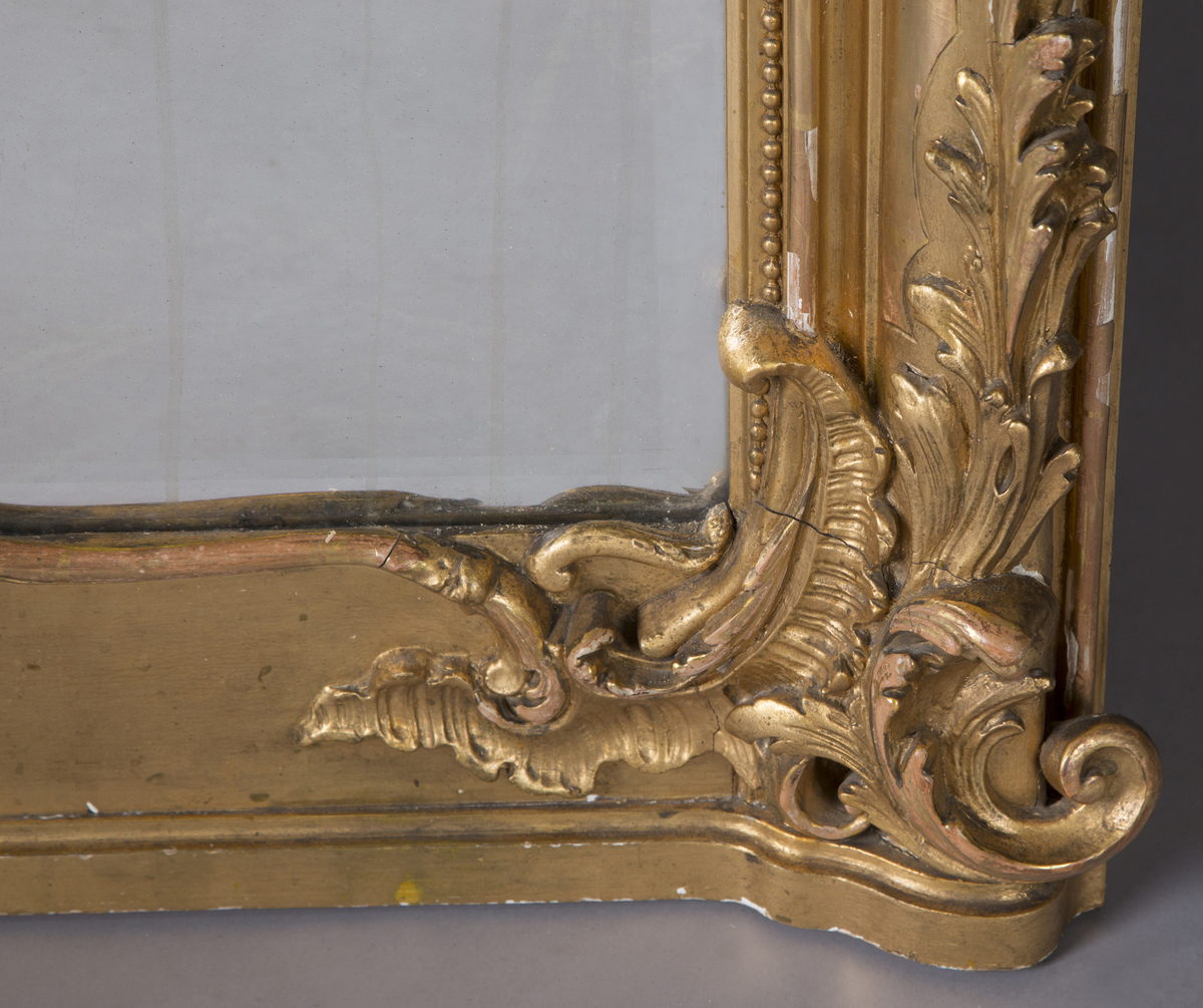 Stort, rektangulært speil med utskjæringer på rammen. Forgylt ramme. Rocailler i asymmetrisk mønster. Speilet buer seg lett ved toppstykket. Rikt asymmetrisk utskjært toppstykke med blomster og rocailler.