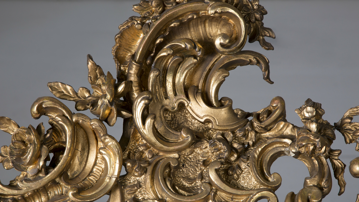 Stort, rektangulært speil med utskjæringer på rammen. Forgylt ramme. Rocailler i asymmetrisk mønster. Speilet buer seg lett ved toppstykket. Rikt asymmetrisk utskjært toppstykke med blomster og rocailler.