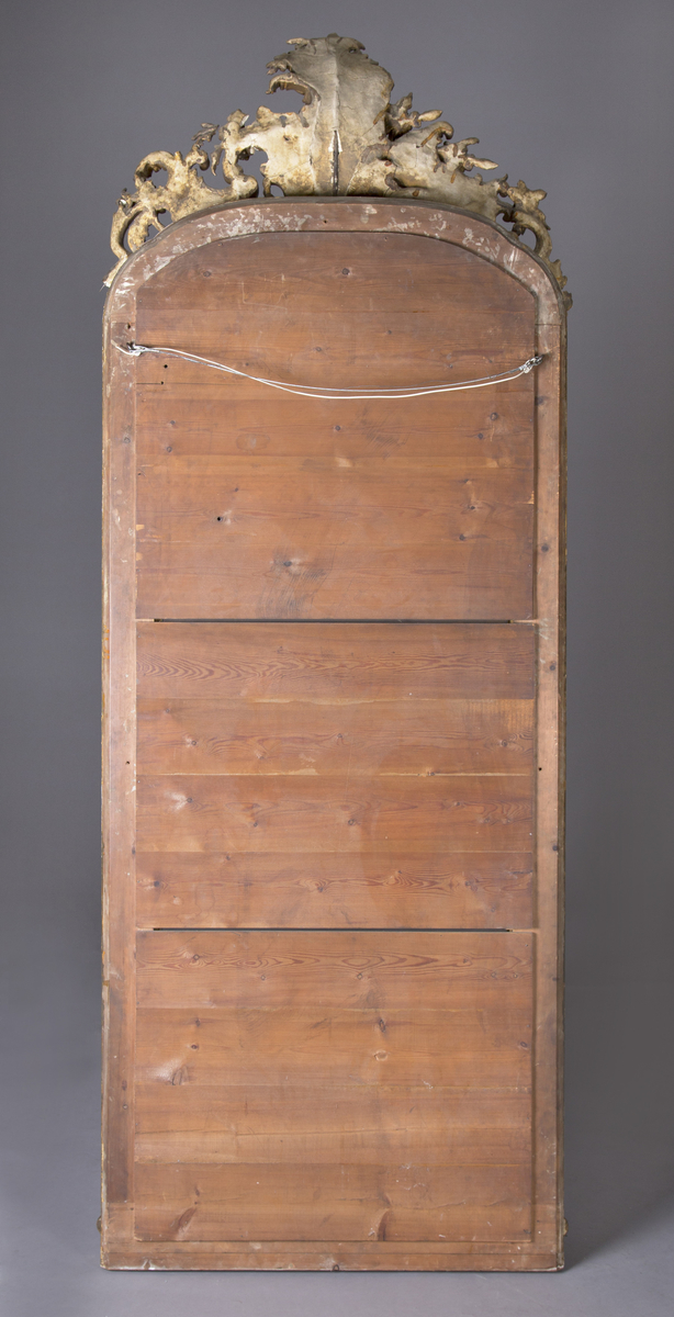 Stort, rektangulært speil med utskjæringer på rammen. Forgylt ramme. Rocailler i asymmetrisk mønster. Speilet buer seg lett ved toppstykket. Rikt asymmetrisk utskjært toppstykke med blomster og rocailler.