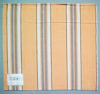 Randigt vävprov i bomull, vävt i tuskaft. Varp i naturvitt, svart, gröngult, gult och grått, inslag i naturvitt. Märkt med påsydd tyglapp med texten: "T. 1216". Vävprovet sitter ihopfästat med snören, med ytterligare tjugoåtta vävprover ( inv.nr 77 - 90, 92 - 100).