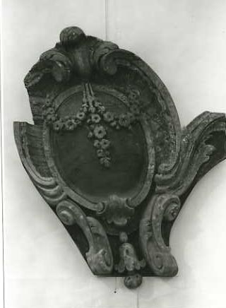 Ovalt ornament. Vit blomranka på svart botten. Snäck- och bladornament . På baksidan påspikad bräda för sammanhållning av lösa delar. Spegelvänd mot O 02343.
