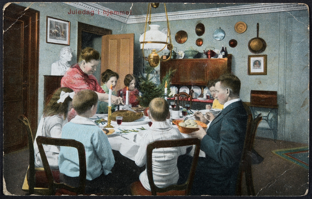 Postkort, julekort. "Juledag hjemme" Familiemiddag, spisestue, interiør. Håndkolorert.