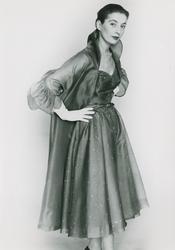 Modell i prickig klänning, kappa, tvåradigt pärlhalsband och