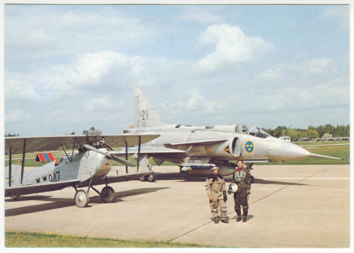 Vykort av flygförare och flygplan J 1 Phönix nummer 947 och JA 37 Viggen märkt -21 / 52 står på flygbana på Malmen. Frankerat med frimärken och stämplat den 9 mars 1976, vid invigningen av Flygvapenmuseum.