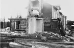 Närmast kameran står skorstensstocken efter brukets äldsta bostadshus. Bortom denna står det mellersta och längst bort det västligast belägna bostadshuset.
Till vänster på bilden skymtar Västra vägen.
Flickan på stegen är fotografens dotter Anna.