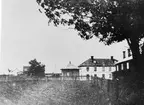 Vy från Brunn 1871.
Bilden tagen från platsen där nuvarande slaktare Petterssons fastighet står. Det mångkantiga huset är spruthuset, stående mitt på torget till mitten av 1950-talet. Det ägs nu av Einar Lundbergs sterbhus. Den vita byggnaden byggdes 1850 av handlanden Hedenström som affärslokal, nu (1985) ägd av Gunder Hedblom och används som bostadshus, tidigare fanns där en läkarmottagning. Högra byggnaden är Norrgårds. Vägen till Rångsta går mellan Norrgårds och staketet. Det instängda området med potatisland är tomten där fotograf Erixons fastighet stod, nu riven med väg över tomten. Huset till vänster finns ingen uppgift om.