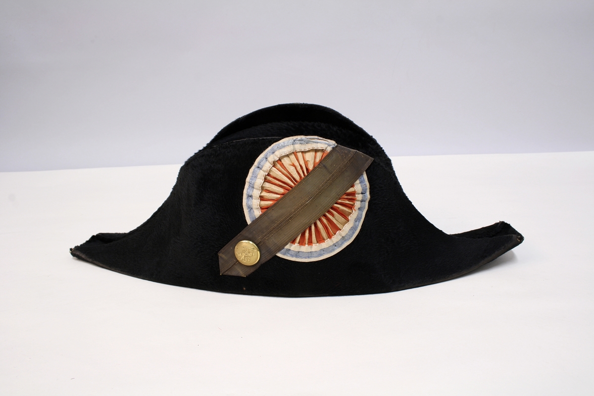 Sort snutehatt med nasjonalkokarde og gullbånd festet med messingknapp med den norske løve.