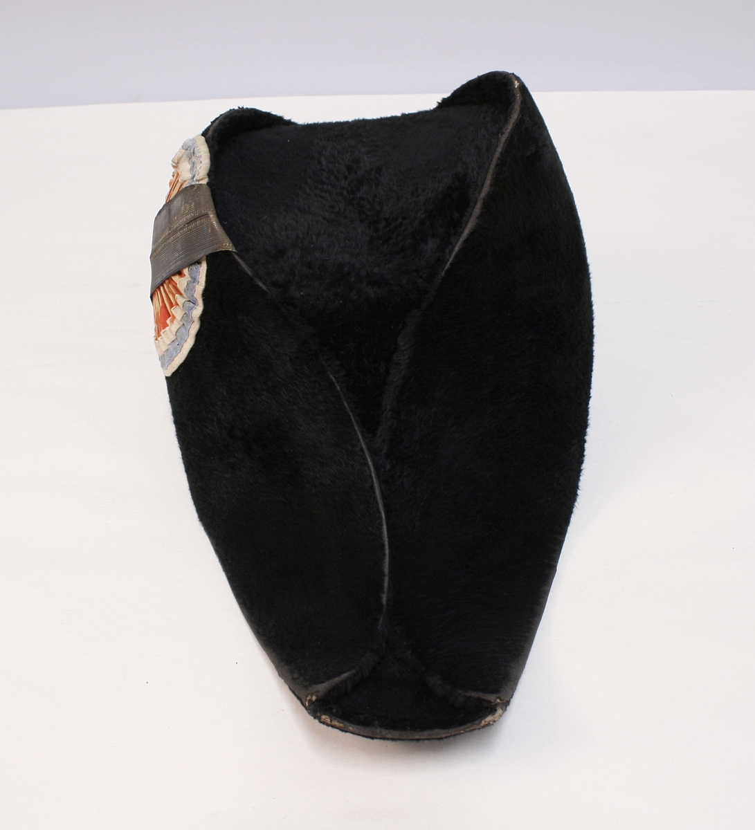 Sort snutehatt med nasjonalkokarde og gullbånd festet med messingknapp med den norske løve.