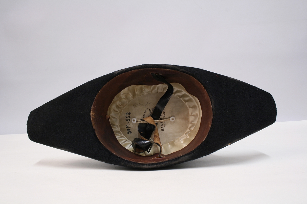 Sort snutehatt med nasjonalkokarde og gullbånd festet med messingknapp med den norske løve.