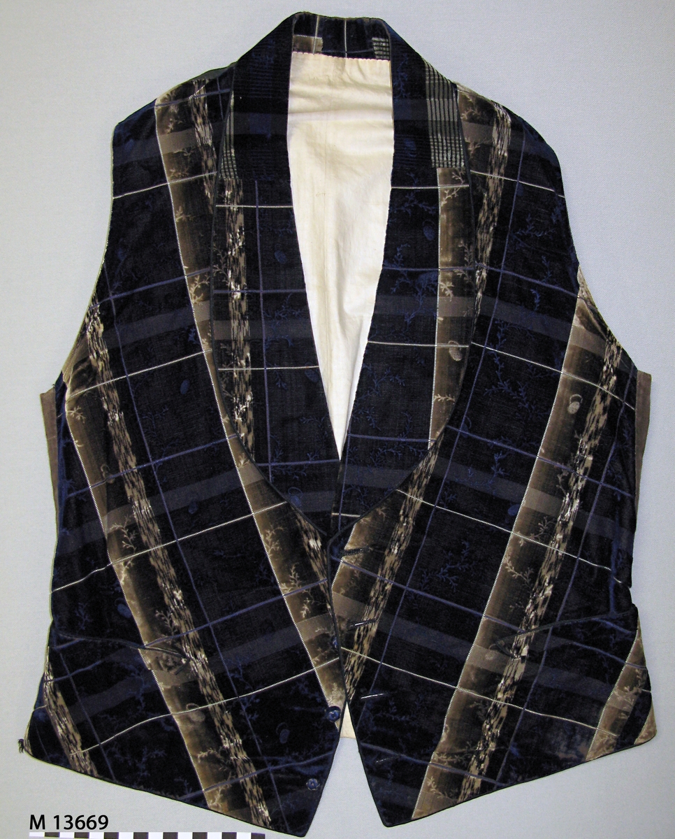 Blå/beige/brun rutig blomranksmönstrad sidensammet. Framsyckena är vadderade. Sammeten är mönstrad i skuren och oskuren sammet med värmeetsad skuren sammetslugg som bildar blomsterrankorna. Ripsbindning bildar rutorna. Vikt skarvad schalkrage och fyra blå trådklädda knappar i silke i öppning framtill. Infällda fickor på båda framstyckena. Tunt svart vaxat bomullstyg i bakstycket med slejf och metallspänne. Helfodrad med ljust linnefoder i tuskaft. Skodd med gröna skinnremsor på insidan av framkanternas nederkant.