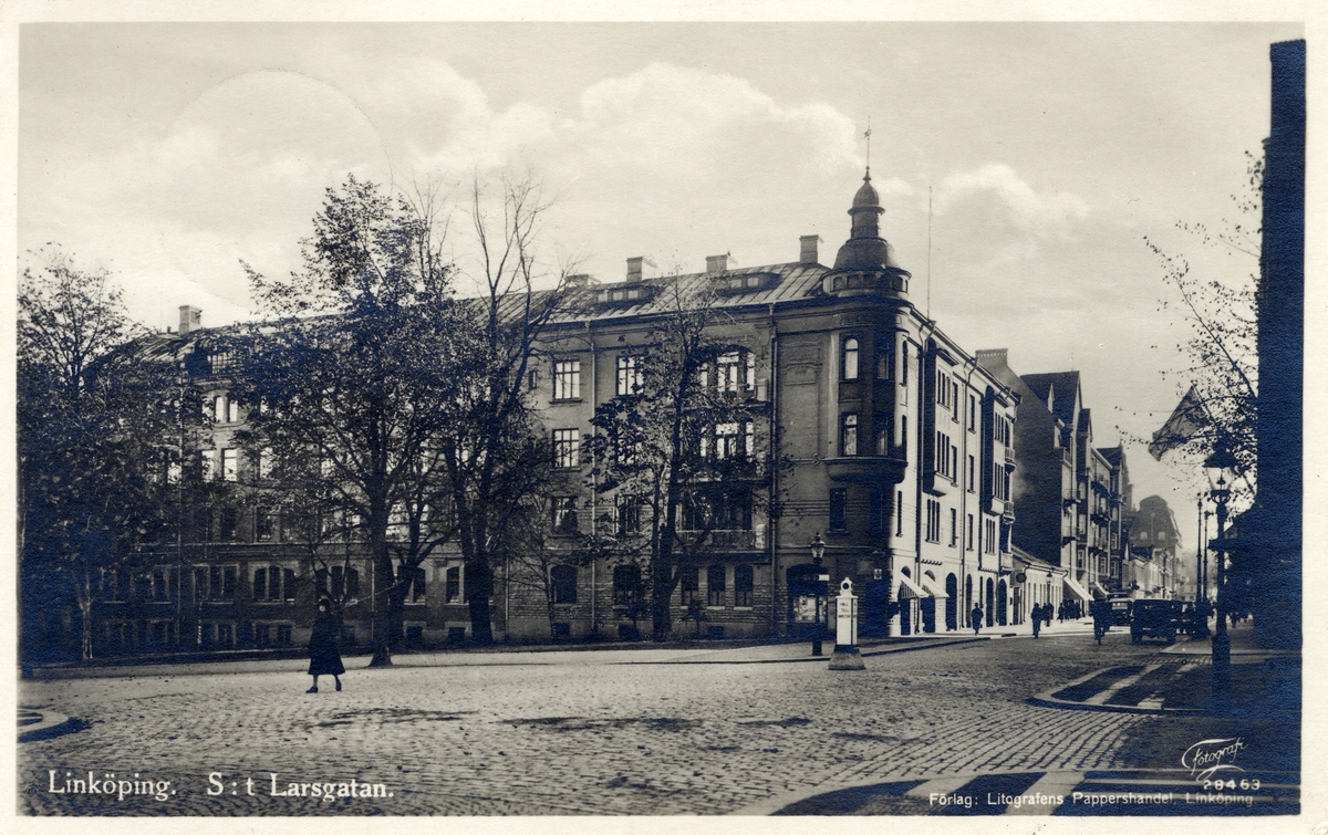 Orig. text:  Linköping. S:t Larsgatan.

S:t Larsgatan sedd söderut, från korsningen med Vasavägen och Järnvägsavenyn.
Byggnaden uppförd 1905 i jugendstil. Byggmästare Oscar Nylander. Arkitekter: Pihlström och Eklund i Norrköping. De gav olika karaktärer åt byggnadens två delar, dels en bostads- och affärsdel, dels en industridel. Industridelen kom att inrymma en fullständig litografisk avdelning, ett boktryckeri, ett bokbinderi och en kartongfabrik.