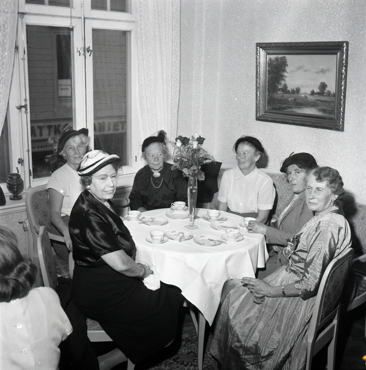 Orig. text: Fru Forsby Centralkondis.
Centralkonditoriet på Hospitalstorget. Flera kvinnor sitter runt ett bord och dricker kaffe. 
Centralpalatset ritades av arkitekten P J Pettersson i Stockholm, men byggmästaren Anders Ohlsson lät dock Axel Brunskog göra nya fasadritningar mot Stora torget. Den fasaden har därför en tydligare jugendkaraktär än vad övriga fasaden har. Byggnaden stod klar 1909.

Extern information: Fotot är taget när fru Maja Forsby, några dagar efter sin sextioårsdag den 26 september 1953, bjöd några väninnor på födelsedagskaffe. Födelsedagsbarnet sitter längst till höger iförd sidenklänning med en blomsterdekoration. I bildens förgrund sitter Celia Göransson, damen i vita blusen vid fönstret är födelsedagsbarnets syster, Inga Wennergren. Damen i svart klänning är domprostinnan Vivi Hammers. Mitt i bild sitter Lisa Thell och bredvid Maja Forsby sitter maria Elisabeth Lisa Carlson.