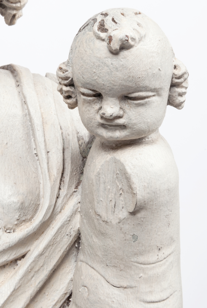 Kyrklig skulptur, trä, staty från gamla korskranket i Heliga Trefaldighets kyrka i Gävle, av Ewert Friis omkring 1665. 

Stående kvinnofigur med naket barn på vänster arm samt stående naket barn vid höger sida. Sistnämnda barn har ett brinnande hjärta i höger hand och kvinnans vänstra hand på sitt huvud. Vänster ben är främst, foten avslagen. Sittande barnets ena ben och andra fot avslagna. 
Fyrsidigt, profilerat postament. 
Gråvit färg.
