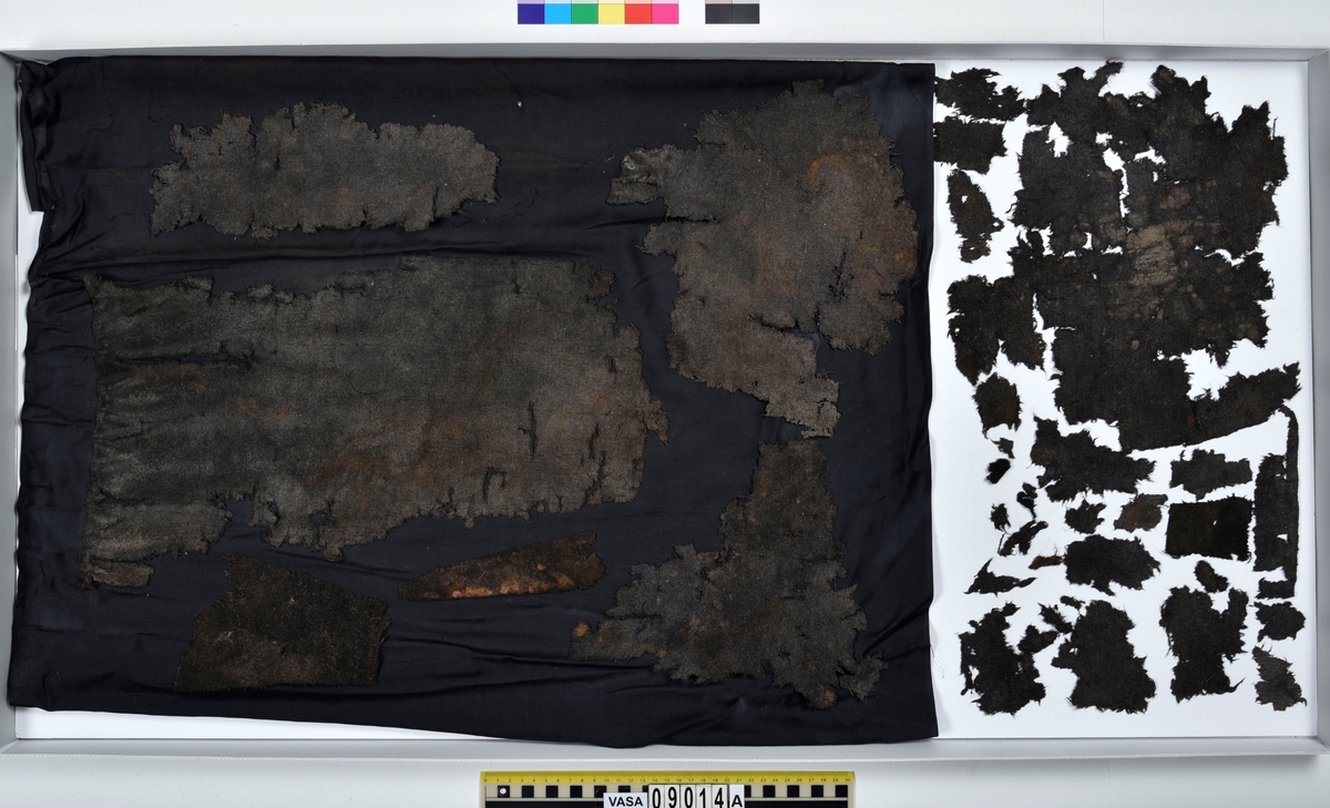 Textildokumentation 2018
Textil, fyndnumret består av mer än 50 st fragment uppdelade på 09014a-h.
Kontextgrupp ÖB20 (övriga fyndnummer i gruppen: 07732, 07762, 09228)
Relaterade fynd: Kontextgrupp ÖB17 och ÖB 18.
.
Fnr 09014a Typnr ÖB20.3:1
Sammanfattning - Ett textilfragment av ull vävt i tuskaft. Färgen är nu mörkbrun, fibrerna varierar i färg vilket tyder på att det är naturfärgad ull. Fibrerna är i vissa partier skadade på ytan och ser därför vita ut. Väven är tunn, jämn och fin och har inga spår av ytbehandling. Fragmentet har tre tillskurna kanter, två av dessa har spår av tre olika sömmar (söm 1: kvicksöm/förstygn). Formen tyder på att det är ett skört till en tröja. Andra delar: Jämför med 07726. 
.
Fnr 09014a Typnr ÖB20.4:1
Sammanfattning - Ett textilfragment av ull vävt i tuskaft. Färgen är nu mörkbrun, originalfärg okänd. I mikroskop ser tyget blåsvart ut. Väven är mycket jämn och slät. I sömsmånen på sida A finns bevarad lugg, på sida B är luggen så välbevarad att bindningen inte syns. Fragmentet har två tillskurna kanter med hål och avtryck av sömmar, även trådrester finns (söm 1: kaststygn - fälld kant, söm 2: ev förstygn - sammanfogande, söm 3: kaststygn - fälld kant). På sida B finns blåfärgad ull och silkesfibrer. 
.
Fnr 09014a Typnr ÖB20.5:1
Sammanfattning - Ett textilfragment av ull vävt i tuskaft. Väven är jämn och tät. En av kanterna är troligen tillskuren, inga sömrester finns. Tyget har inga spår av ytbehandling. På ytan finns en del bastfibrer. Relaterade fynd: Vävens struktur liknar ÖB20.4:1 men tygerna har ändå olika karaktär och detta fragment saknar lugg. 
.
Fnr 09014a Typnr ÖB20.6:1
Sammanfattning - Ett textilfragment av ull vävt i tuskaft. Färgen är nu brun, originalfärg är okänd men möjligen naturfärgad, fibrerna är mycket släta och varierar i färg från brun till nästan svart. Fragmentet är litet och mycket skadat, endast några få bindepunkter återstår vilket försvårar mätningar. 
.
Fnr 09014a Typnr ÖB20.7:1
Sammanfattning - Ett textilfragment av  ull vävt i tuskaft. Färgen är svartbrun, originalfärg okänd men möjligen naturfärgad då fibrernas färg varierar. Inga tydliga spår av ytbehandling. Väven är jämn men garnet är hårt spunnet vilket ger tyget en kypertkaraktär (falsk kypert). Fragmentet har inga tillskurna kanter eller sömmar. På ytan finns enstaka vita silkesfibrer.
.
Fnr 09014a Typnr ÖB20.8:1
Sammanfattning - Ett textilfragment av ull. Fragmentet är mycket litet och dåligt bevarat så bindningen är svår att avgöra, troligen 2/2 kypert. Färgen är svart, möjligen naturfärgad ull då fibrerna varierar något i färg. Tyget har ingen synlig ytbehandling. Garnet är hårt spunnet vilket ger tyget en speciell karaktär. 
.
Fnr 09014b Typnr ÖB17.1:8-11
Sammanfattning - Fyra textilfragment av ull vävt i tuskaft. Färgen är mörkbrun, originalfärg okänd men den bruna tonen slår mot röd. Tre av fragmenten har tillskurna kanter och spår av sömmar. Andra delar, som troligen kommer från samma tröja, är fnr 03261a och d, 09014h samt 09228a. 
Fragment ÖB17.1:9 - Fragmentet har två tillskurna kanter varav den ena har spår av en söm. Fragmentet är troligen sidostycket till en tröja. Den tillskurna kanten har då varit monterad mot tröjans bakstycke och bör ha hört samman med fyndnummer 03261d, vilket är ett bakstycke till en tröja.
Fragment ÖB17.1:10 - Fragmentet är mycket skadat men är troligen av typen ÖB17.1. Formen är densamma som för del av fragment ÖB17.1:9 och kan därför vara en dubblering av detsamma, alternativt det motstående sidostycket.
.
Fnr 09014c Typnr ÖB20.9:1-19
Sammanfattning - Nitton textilfragment av ull vävt i tuskaft. Färgen är brun, originalfärg okänd. Sida B har en kort tät lugg som döljer bindningen. På sida A finns ingen lugg och bindningen är synlig. Fjorton av fragmenten har tillskurna kanter och sömmar. Tre av fragmenten har sydda knapphål. Flera fragment är dräktdelar, till exempel finns en fragmentarisk krage. På ytan på flertalet fragment finns fibrer i flera klara färger, till exempel rosa, röd och blå. Vita fibrer finns i stor mängd, kan vara recenta.

Fragment ÖB20.9:1 - Fragmentet har flera tillskurna kanter med avtryck och hål efter olika typer av sömmar (söm 1: ev. sammanfogande, söm 2: kaststygn - fåll, söm 3: kaststygn - sammanfogande, söm 4: kaststygn - sammanfogande, söm 5: osäkert, söm 6: osäkert), trådrester finns. Kanterna och sömmarnas karaktär gör att sida A bedöms vara plaggets rätsida/utsida. Några hål som ej är stygnhål men kan vara original finns. I fragmentet sitter fast två stycken silkestrådar (söm 7: silkestråd med knut, fäst i tyget, söm 8:  silkestråd med ögla, fäst i tyget). Det är samma typ av tråd som knapphålen på fragment ÖB20.9:2 är sydda med. På sida A finns ett område med extra mycket korrosion och även en långsmal vitaktig avlagring.

Fragment ÖB20.9:2 - Fragmentet har inga bevarade tillskurna kanter, dock finns en någorlunda välbevarad rad med knapphål. Samtliga knapphål är trasiga i ena sidan så deras ursprungliga storlek går ej att avgöra. Knapphålen är sydda med knapphålsstygn i silkestråd och sitter med 13-15 mm mellanrum (c/c mått). Det tvärställda tränsen består av ca 10 stygn och syns ej på sida B, tränsens knutar sitter vända från knapphålet. På sida B anas rester av bastfiber under knapphålsstygnen, troligen från en dubblering av tyget eller ett foder. 

Fragment ÖB20.9:3 - Fragmentet har fyra stycken knapphål, varav ett är helt. Knapphålen är skurna på skrådden. Eventuellt finns spår av en söm längs en del av kanten. Knapphålsstygn och trådrester är mycket fragmentariska.

Fragment ÖB20.9:4 - Fragmentet har tre stycken knapphål.  Knapphålen är sydda med knapphålsstygn i silkestråd. Knapphålens längd är 19-20 mm och de sitter med 18-22 mm mellanrum (c/c mått). Eventuellt är fragmentets ena kant en sömsmån, kan ha varit monterad mellan andra tyglager (kanten har avvikande färg). Under knapphålsstygnen på sida B finns rester av annat material, eventuellt bastfiber. Bastfibrer finns också utspridda över ytan på sida B, kan vara rester av en dubblering till tyget eller ett foder, se fragment 9:2. På sida A finns avlagringar och korrosion. 

Fragment ÖB20.9:5 - Fragmentet har bristningar i tyget som ser ut som knapphål, dock finns inga rester av stygnhål eller tråd. Fragmentets ena kant är troligen en sömsmån, kan ha varit monterad mellan andra tyglager (kanten har avvikande färg). Enstaka spår av söm och tråd finns längs kanten (söm 1), dessa är mycket otydliga. På fragmentets andra (mycket trasiga) kant finns ett mycket tydligt stygnhål. Fragment 9:4 och 9:5 ser ut att kunna höra ihop, dock går trådsystemen åt olika håll så det är inte fallet.

Fragment 9:6-9 - Till det stora fragmentet 9:6 hör det lilla lösa fragmentet 9:7. I fragment 9:6 sitter två fragment fastsydda, 9:8 och 9:9. De sammansydda fragmenten har tre tillskurna kanter och spår av minst fem sömmar (söm 1: kaststygn, söm 2: förstygn el. liknande - sammanfogande, söm 3: kaststygn, söm 4: sammanfogande, fäster ihop 9:6 med 9:8 och 9:9, söm 5: två stygnhål), trådrester finns. Det är troligt att 9:8 och 9:9 är delar av samma tillskurna bit, och att den utgjort en dubblering till 9:6 (inklusive 9:7). Den tillskurna formen ser ut att vara en krage. Fragmentet skulle då vara en halv krage, bevarad från framkant till nästan mitt bak. På sida A finns en beläggning på delar av ytan. På sida B finns en mängd fibrer i klara färger: blå, vit, rosa, tegelröd, orange, karminröd, grön, mörkgul och grå. fibrerna ligger ytligt med nästan samtliga sitter delvis fast i tygets lugg eller har en eller båda ändar nere i vävens bindning. Fibrerna bör därför vara ursprungliga. Sida A har en mindre mängd av nämnda fibrer, mest förekommande på ytan av fragment 9:8 och 9:9.

Fragment ÖB20.9:10 - Fragmentet har två tillskurna kanter. Dessa är invikta mot sida B som en 6-7 mm bred fåll som är fastsydd med kaststygn, trådrester finns (söm 1 och 2). Fragmentet kan vara ett skört till en tröja. På båda sidors yta finns fibrer i klara färger: grå, ljusblå, orange, orangebrun, vitgul, blå svart, vit, röd, korallröd och rosa.

Fragment ÖB20.9:11 - Fragmentet har tre tillskurna kanter med sömmar. Två av kanterna är invikta och fastsydda mot sida B, som fållar (söm1: kaststygn - fåll, söm 2: kaststygn - fåll). Stygnen går ej igenom till sida A men sömmen syns som bucklor i fragmentets yta. Söm 3 längs den tredje kanten har troligen varit en sammanfogande söm sydd med kaststygn. Stygn och trådrester finns bevarade från samtliga sömmar. Under fållen vid söm 1 finns ett litet fragment av en annan textiltyp. Troligen ursprungligen en dubblering eller liknande. Fragmentet är ca 10x5 mm stort och har fått typnummer ÖB20.16:1. På ytan på sida B finns enstaka bastfibrer.

Fragment ÖB20.9:12 - Fragmentet har två tillskurna kanter med sömmar (söm 1: ev kaststygn, söm 2: osäker). Vid söm 2 är sömsmånen vikt mot sida B. Vid söm 1 är kanten inte vikt. Fragmentet har samma form som ÖB20.9:6, "kragen".

Fragment ÖB20.9:13 - Fragmentet har två tillskurna kanter med sömmar (söm1: sammanfogande, söm 2: osäkert). De två övriga kanterna är eventuellt också de tillskurna men spår av eventuella sömmar är för otydliga. Enstaka fibrer med klara färger (rosa, blå, vit) finns på båda sidor, fler på sida B. Vid söm 2 finns på ett ställe en fiberknippa som kommer upp ur vävens bindning, kan vara rester av en tråd och är eventuellt halsplat silke. 

Fragment ÖB20.9:14 - Fragmentet har en tillskuren kant med söm (söm1: ev sammanfogande). I stygnhålen finns rester av tråd.
.
Fnr 09014c Typnr ÖB20.10:1
Sammanfattning - Ett textilfragment av ull vävt i tuskaft. Färgen är brun, originalfärg okänd. Sida B har en kort och tät lugg, bindningen syns bara på sida A. Längs ena kanten finns tre stycken tydliga hål. Hålen är gjorda med ett verktyg som skär av fibrerna snarare än tränger undan dem.
.
Fnr 09014c Typnr ÖB20.16:1
Sammanfattning - Fragmentet är mycket litet och sitter inuti den invikta fållen på fragment 09014c ÖB20.9:11, det sticker bara fram någon millimeter. Fragmentet är mycket skört. Bevarandegrad och storlek gör mätningar svåra. Det är olika garn i trs 1 och trs 2. Sida B är täckt av en lugg, på sida A syns bindningen, om än fragmentariskt.
.
Fnr 09014d Typnr ÖB18.16:2-8
Ej dokumenterad
.
Fnr 09014d Typnr ÖB20.11:1-2
Ej dokumenterad
.
Fnr 09014e Typnr ÖB20.12:1-4
Sammanfattning - Fyra textilfragment av ull vävt i tuskaft. Färgen är brun med inslag av täckhårsfibrer i en mörkare brun färg, originalfärg okänd. Fragmenten är mycket fragmentariska med trs 1 bättre bevarat än trs 2. Enbart på en del av fragment ÖB20.12:1 finns trs 2 samt bindningen bevarad. Utspridda över tygets yta finns grova bastfibrer samt korrosionsfläckar. 
.
Fnr 09014f Typnr ÖB20.13:1
Sammanfattning - Ett textilfragment av ull vävt tuskaft. Färgen är mörkbrun, fibrerna varierar mellan ljus och mörk brun. Originalfärg okänd, möjligen naturfärgad ull. Garnet är hårt spunnet vilket ger väven en särskild karaktär, sida A har en mer strukturerad ytan än sida B. Fragmentet har inga tillskurna kanter. På sida A finns enstaka röda och gulgröna silkesfibrer, samt bastfibrer. På sida B finns enstaka blå, vita och rosa silkesfibrer.
.
Fnr 09014g Typnr ÖB20.14:1-3
Sammanfattning - Tre textilfragment av ull och bastfiber vävt i tuskaft. Färgen är beige för bastfibern (trs 1) och svartblå för ullen (trs 2). Trs 2 är mycker grövre än trs 1. Trs 1 är nästan helt försvunnet. Två av fragmenten har tillskurna kanter och ett har spår av en sömsmån. På ytan av fragmenten finns en stor mängd bastfiber samt en vit/rosa tuss med silke. På fragment 14:2 finns några intensivt blå ullfibrer.
.
Fnr 09014h Typnr ÖB17.1:12-13
Sammanfattning - Två textilfragment av ull vävt i tuskaft. Färgen är brun, originalfärg okänd. Det större fragmentet är tillskuret och har spår av sömmar. Fragmentet är en ensömsärm med sömmen placerad mitt bak på ärmen. På ytan finns stora rostfläckar. Andra delar: Hör troligen (trots färgskillnad) till skelettet Beatas tröja, se fnr 03261a-d, 09228a, 09014b och h.
