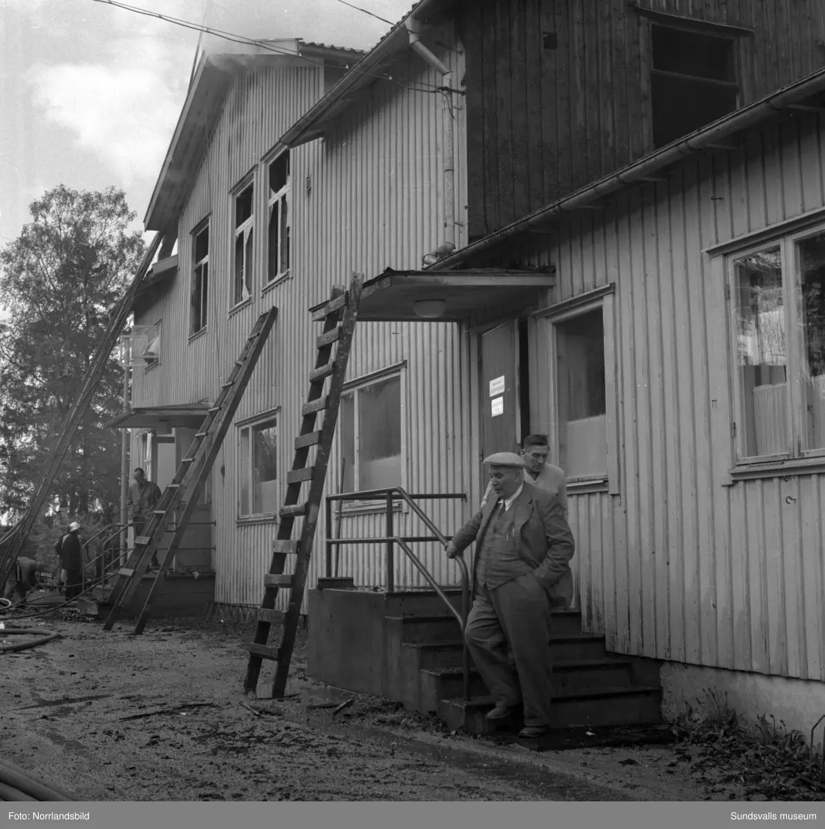 En stor serie bilder från en eldsvåda i kontorsbyggnaden och Bylanders Café vid Luckstaverken, Lucksta ångsåg. Släckningsarbete pågår och massor av människor hjälps åt att rädda så mycket lösöre som möjligt. Elden startade i på övervåningen i kassören Sven Perssons bostadslägenhet. Persson räddade sig ut genom att hoppa från balkongen på baksidan. Brandkårerna från Attmar, Tuna och Sundsvall lyckades till slut få bukt med elden men övervåningen totalskadades och det kafé som fanns inrymt i bottenvåningen fick stora brand- och vattenskador.