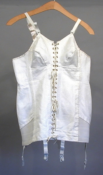 Korsett med snörning framtill. Fyra strumpeband. Material: Textil, ull, bomull, syntetmaterial.