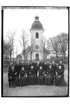 Rinkaby kyrka i bakgrunden.
Konfirmander, 14 ungdomar och prästen
Byggnader.