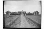 En bostadshus, två ekonomibyggnader, en kvinna.
Gustaf Kolmodin.