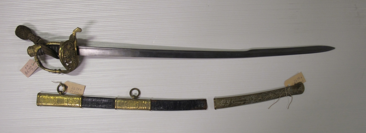 Balja til sjöofficerssabel (O 02634.A) av svartlackerat läder med tre stycken förgyllda och cicilerade beslag. Det översta med lilla riksvapnet, ankare, sponton samt ring. Det mellersta med akterspegel och kampanlykta och ring för koppel. Det understa med drake, spjut, bladverk, ankare, kanon, gevär och hillebard samt nya gösen (efter 1844).
