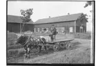 Tjur spänd framför flakvagn.
Ekonomibyggnader i bakgrunden.
Karlsson
Norensberg, Örebro.