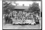 Hidingsta skola, skolbarn med lärare.
Kantor K.E. Håkansson
Envånings skolobyggnad i bakgrunden.