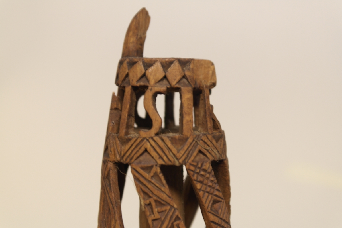 Nøstepinne i skåret furu. Skåret ut med snodde spiler smykket med geometriske mønstre. Øverst på pinnen er det skåret ut, slik at bokstavene står fritt.