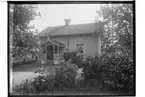 En och en halvplans enkelstuga med veranda i snickarglädje.
Äldre par framför huset.
A. Edlund