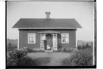 Envånings bostadshus med veranda.
Ett par med ett litet barn på verandan.
Samuel Karlsson.