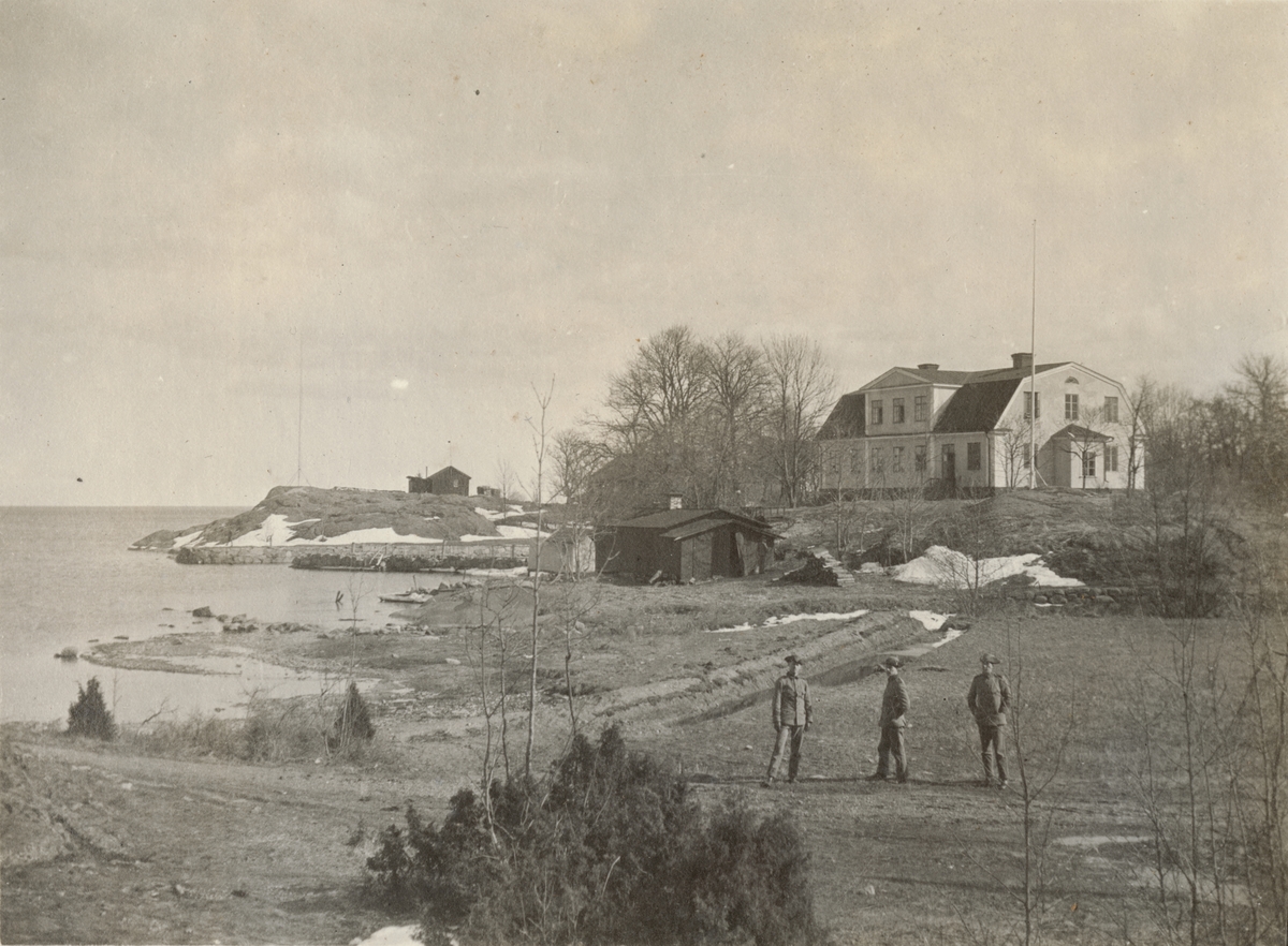 Kustlandskap med trähus och tre soldater.