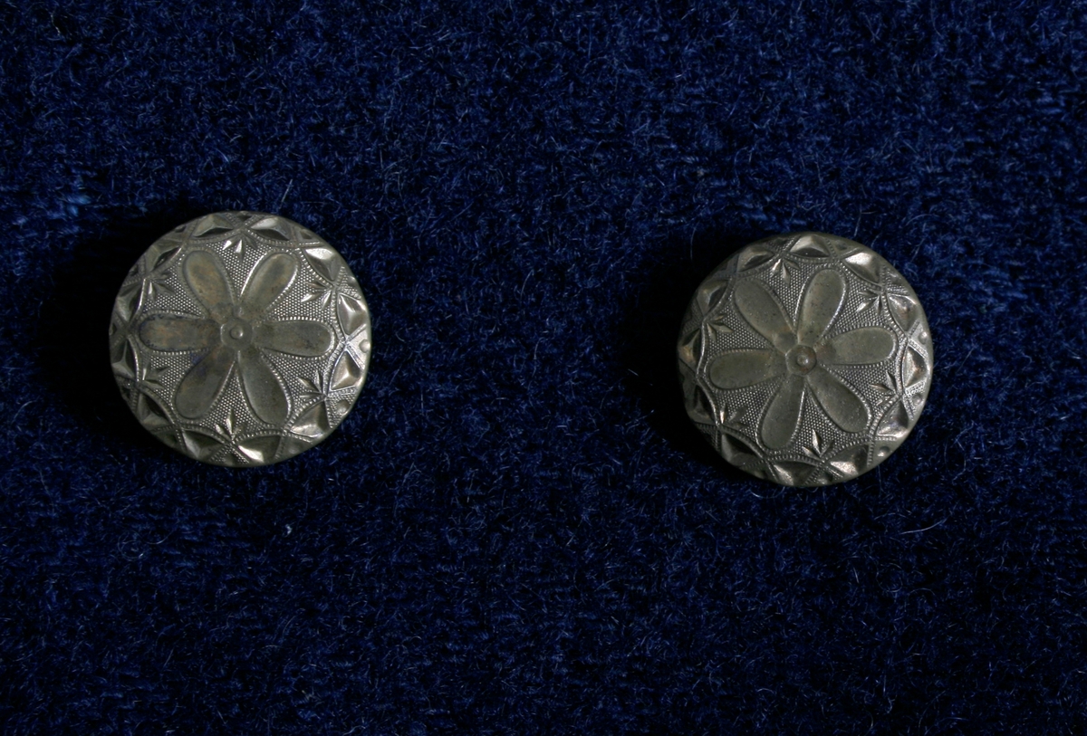 Kort trøye i mørk blått ullstoff, kypertvevd. Overkrage i mørk grønt ullstoff. Underkrage og slagene er mørkeblå. Trøyen er dobbeltspent med buet knappestilling 6 x 2. Den lukkes bare med 2 knapperKnappene er preget med en blomst i midten og en ytterkant av trekanter. På framstykket er det 2lommeklaffer, men bare 1 lomme foret med ubleket linstoff. Kun framstykket er foret. Sidesømmer og skuldersømmer er bakovertrekte. Trange tosømsermer med mansjetter som har 2 messingfargede knapper og 2 knapphull. Stikninger rundt kragen, slagene, MF og nedre kant av trøyen. Høyre undererme er skjøtt oppe ved ermhulen og nede ved mansjetten.