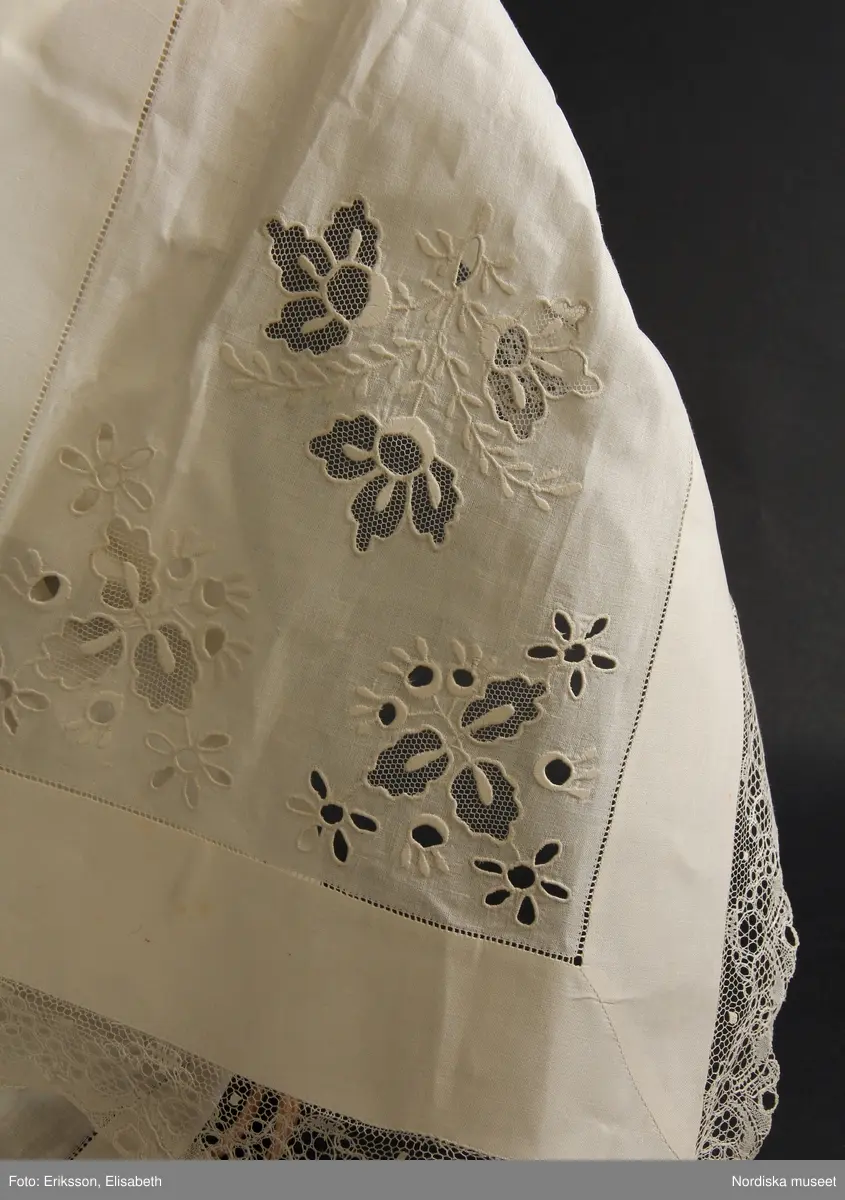 b. Brudtröja av svart vadmal,  Runt alla kanter bård av ytterst brunsvart sammetsband och innanför ett 4 cm brett svart sammetsband  med invävt bladmönster. På ärmarna ett svart slätt sammetsband med pålagd guldspets därefter siden band i rosa och grönt på botten av  svart  sammet och överst i bården en knypplad guldspets. 
c: Förkläde. Material: Textil, bomull. Teknik: Manufakturvävning. Handsömnad. Längd: 77 cm. Bredd: 110 cm. Färg: Vit.
Förkläde i vitt manufakturvävt bomullstyg, ihopsytt i mitten, smalrandigt, stärkt. Rynkningar mot midjelinning i tuskaftat bomullstyg, 1,5 cm bred, fastsydda bomullsband i sidorna. Uppvikt fåll nedtill, 6,5 cm, ovanför fåll, 5 lagda veck med ca 1 cm mellanrum, enkel utdragssöm i kanten av vecken.
/Inga-Lill Eliasson 2008-02-25

e: Krage. Längd: 47,5, cm - totallängd, bröststycke. Bredd: 33 cm - bröststycke. Höjd: 14 cm - kraghöjd, inkl spets. Material: Textil, bomull. Lingarn - spets. Bomullsgarn - broderi. Teknik: Tuskaft. Vitbroderi, Knyppling. Handsömnad.
Krage i tuskaftat vitt bomullstyg. Rektangulär duk, uppklippt halshål med fastsydd krage, 14 cm hög. Kragen har 3,5 cm bred fåll, enkel utdragssöm i kanten. Vitbroderi  i framkant,  plattsöm och kantsydda hål med infällt tyll, två sydda knapphål. Handknypplad spets fastsydd på långsida och korstsidor, 2,5 cm bred. Öppning fram, 24 cm långt sprund. Kragen är handsydd.
Lästips: Svensson Sigfrid, (1935). Skånes Folkdräkter, en dräkthistorisk undersökning 1500 - 1900. Stockholm: Nordiska Museets Handlingar: 3.
/Inga-Lill Eliasson 2008-02-19