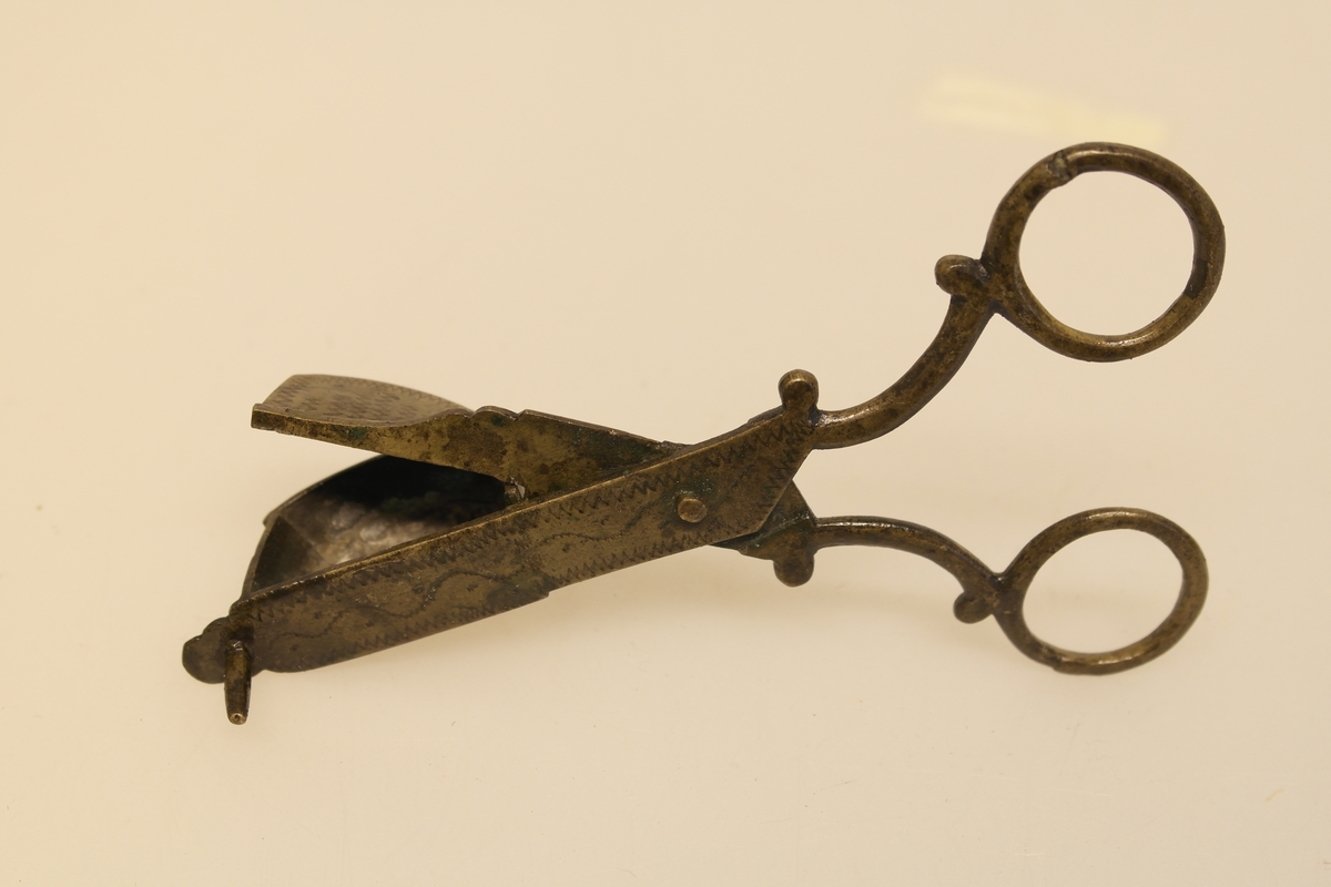 Lyssaks i støpt, pusset og siselert messing. Inngravert ornamentikk: sikksakk og bølgeborder.