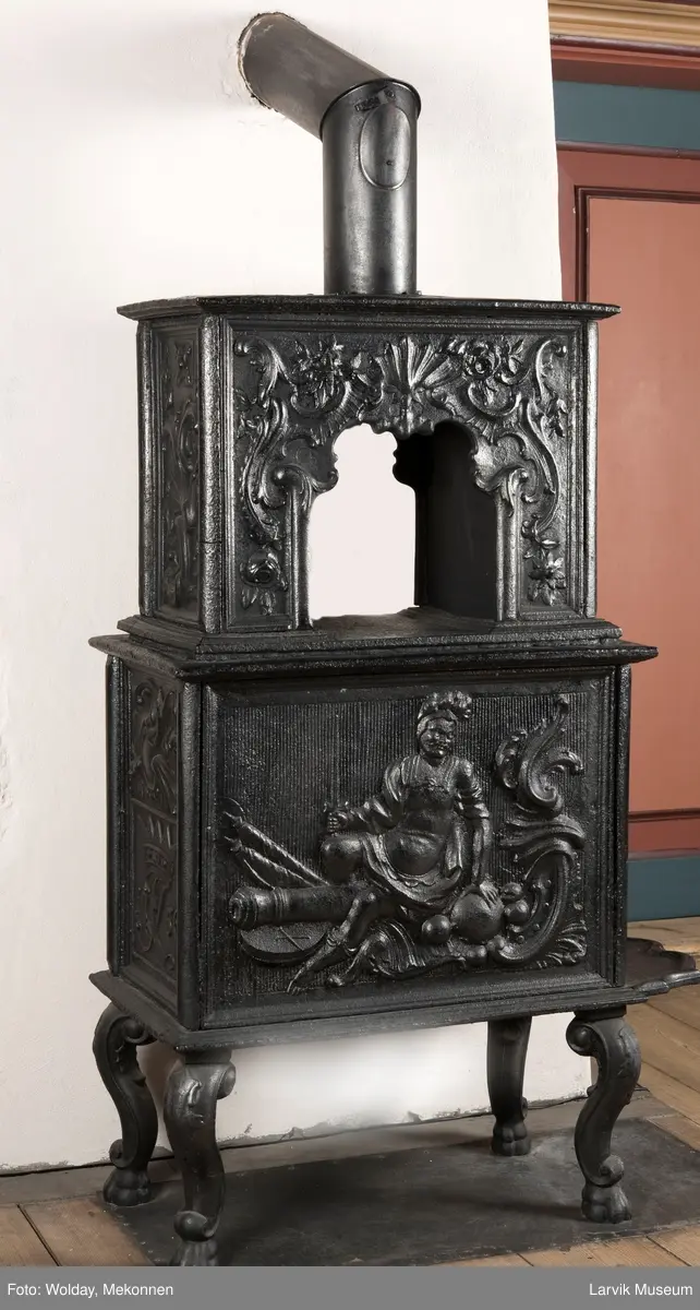 Ovn i  2 etasjer. 
Rokokko, jfr. nr 411 i Norsk Jernskulptur b II 
1. etasje langside: Mars sitter på en kanon med sverd i høyre hånd. Riflet bunn.
1 etasje kortside: Øverst: Rokokko-ornament, nederst: Grevekrone monogram. FL og 1756 
nederst: ovnsdør 2 hengsler ovalt askebrett med profilert kant.
2.etasje langside: Fyldig rokokko-ornament. med blomster. Uregelemessig portalåpning. 
2. etasje kortside: Rokokko-ornament, 
Ovnen har sungne ben m/dyreføtter
