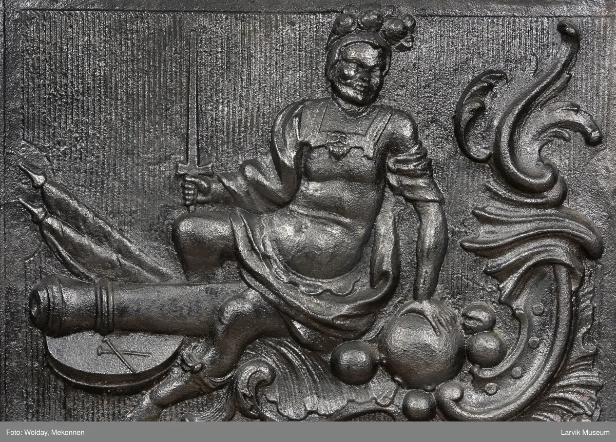 Ovn i  2 etasjer. 
Rokokko, jfr. nr 411 i Norsk Jernskulptur b II 
1. etasje langside: Mars sitter på en kanon med sverd i høyre hånd. Riflet bunn.
1 etasje kortside: Øverst: Rokokko-ornament, nederst: Grevekrone monogram. FL og 1756 
nederst: ovnsdør 2 hengsler ovalt askebrett med profilert kant.
2.etasje langside: Fyldig rokokko-ornament. med blomster. Uregelemessig portalåpning. 
2. etasje kortside: Rokokko-ornament, 
Ovnen har sungne ben m/dyreføtter