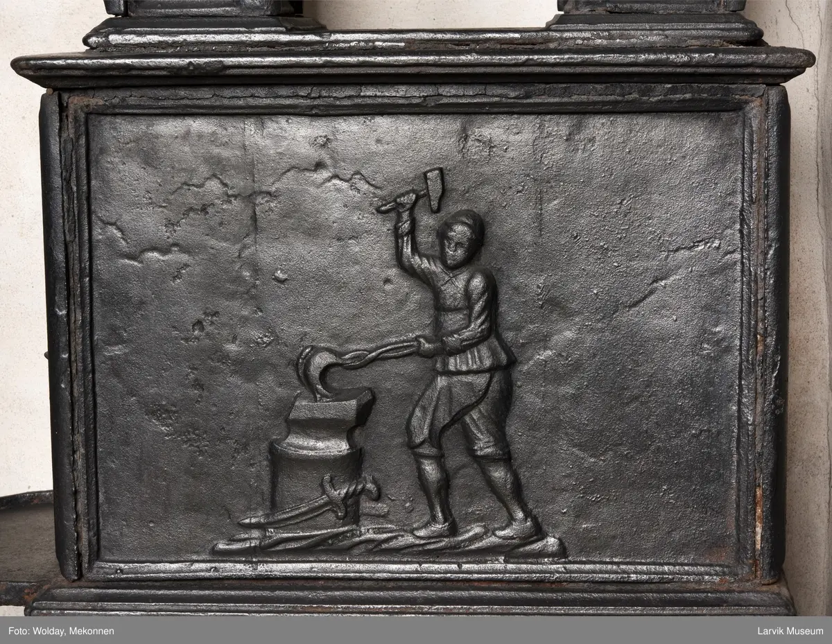 Jernovn med to etasjer, begge er rektangulære. Ovn står på muret fot/understell.
1etasje langside: Vulkan som smed .
1etasje kortside: Musling. 
2etasje langside: Buet åpning i profilert innramming omgitt av girlander. 
2etasje kortside: Overflødighetshorn.