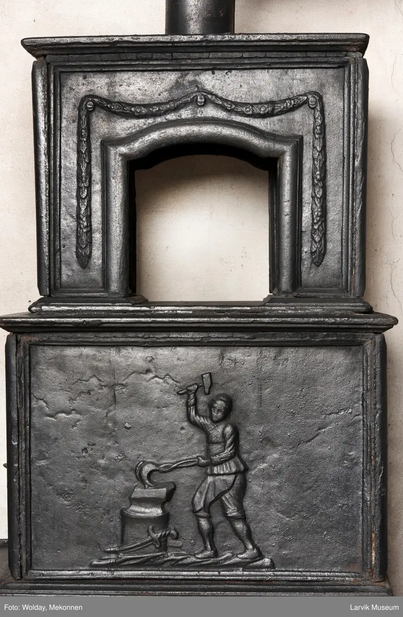 Jernovn med to etasjer, begge er rektangulære. Ovn står på muret fot/understell.
1etasje langside: Vulkan som smed .
1etasje kortside: Musling. 
2etasje langside: Buet åpning i profilert innramming omgitt av girlander. 
2etasje kortside: Overflødighetshorn.